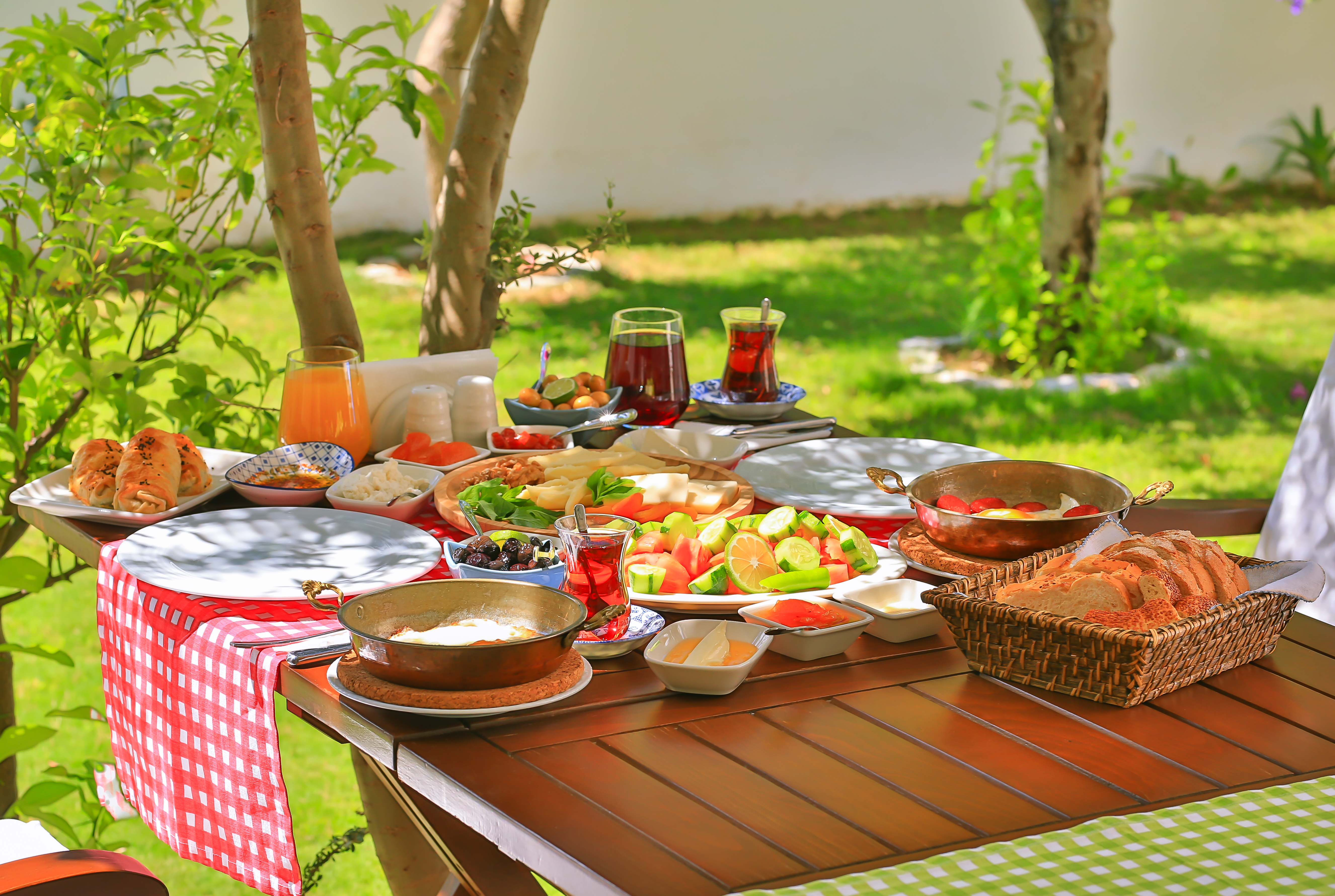 Ağaçların gölgesinde çay, peynir, zeytin ve sıcaklarla kahvaltı sofrası